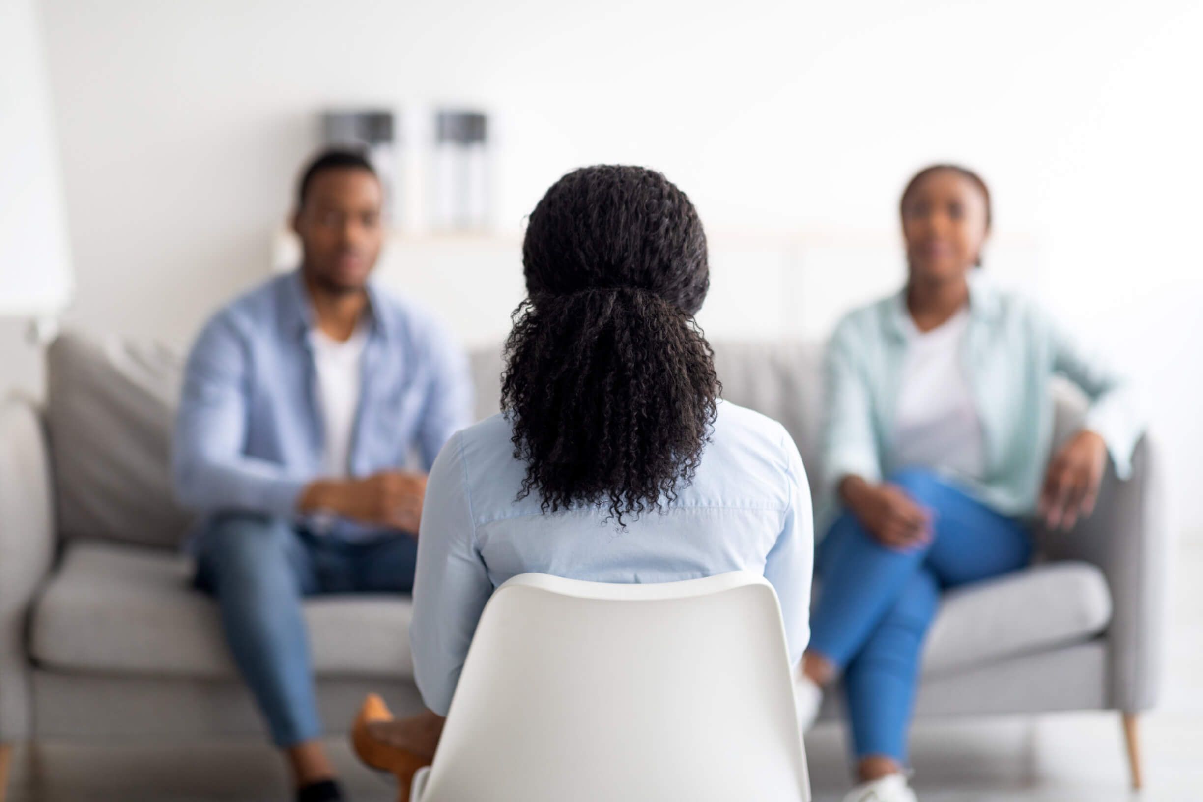 Female psychologist sitting with her back to camera, consulting millennial black couple at office